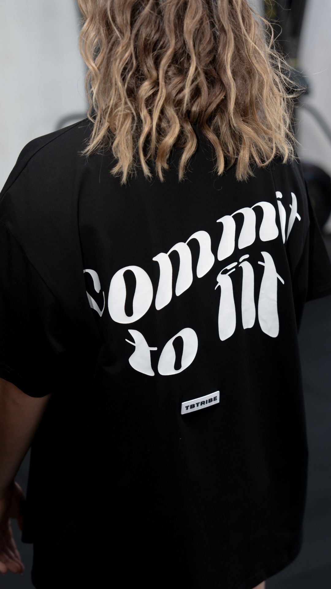 Male and Female model wearing a black oversized t shirt with white writing on the front and back that reads Commit to Fit